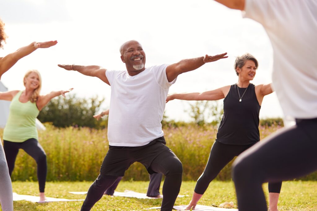 Female Teacher Leading Group Of Mature Men And Women In Class At Outdoor Yoga Retreat